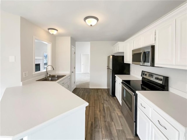 kitchen with light countertops, appliances with stainless steel finishes, dark wood-style floors, white cabinets, and a sink