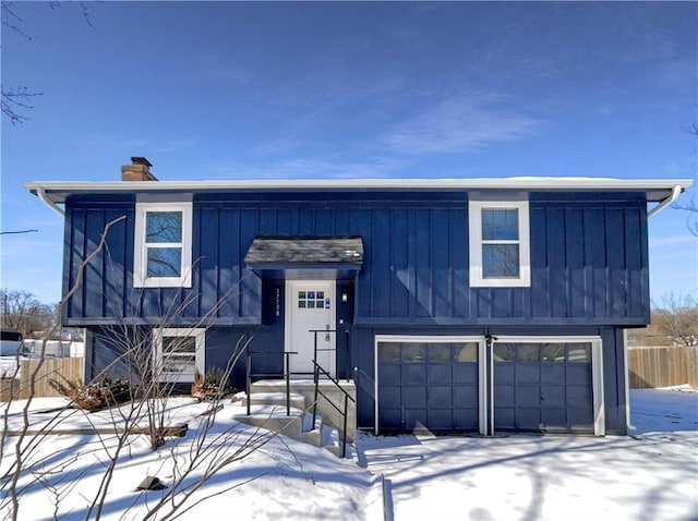 view of front facade featuring board and batten siding, a chimney, a garage, and fence