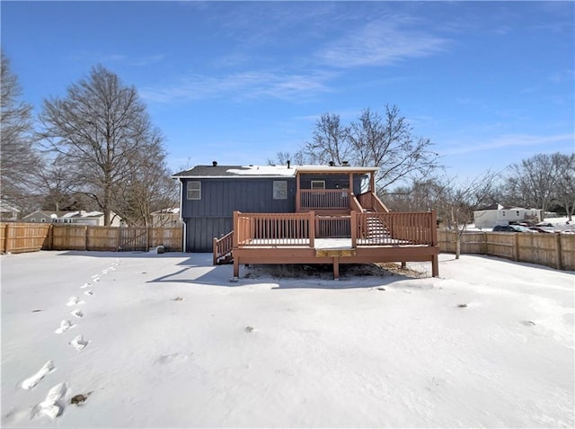 snow covered property featuring a deck, board and batten siding, and a fenced backyard