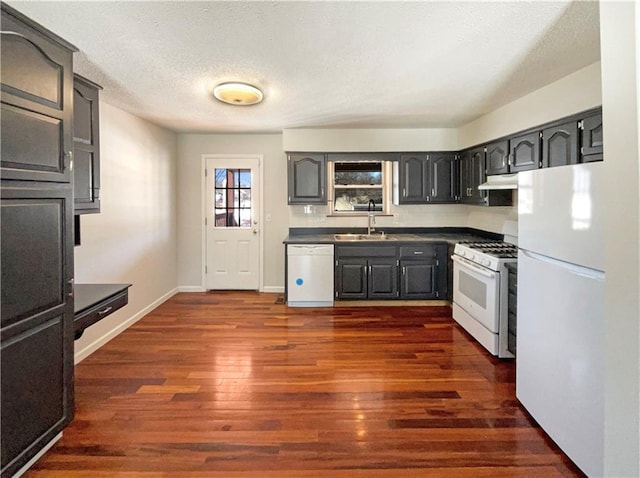 kitchen featuring white appliances, dark wood-style floors, a sink, under cabinet range hood, and dark countertops