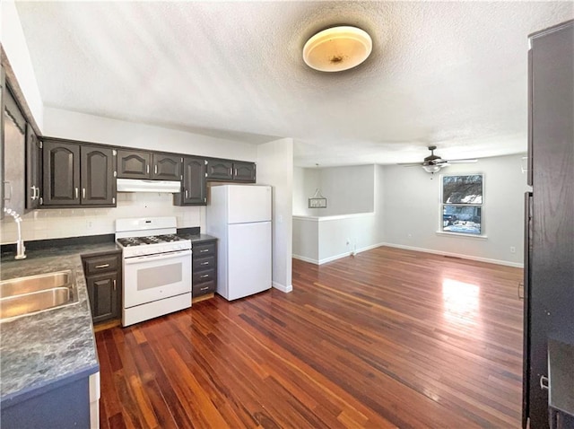 kitchen with under cabinet range hood, backsplash, dark countertops, white appliances, and dark wood-style flooring