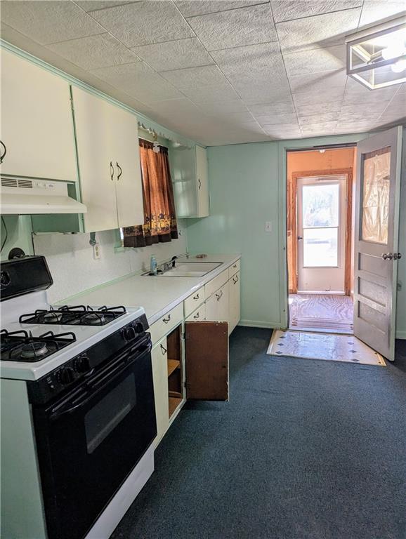 kitchen with under cabinet range hood, a sink, range with gas cooktop, light countertops, and dark colored carpet