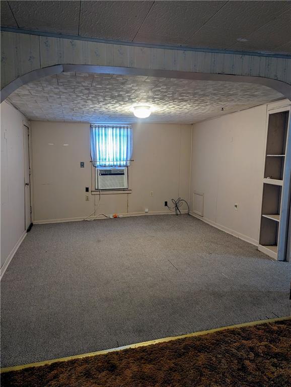 basement featuring cooling unit, arched walkways, carpet, and baseboards