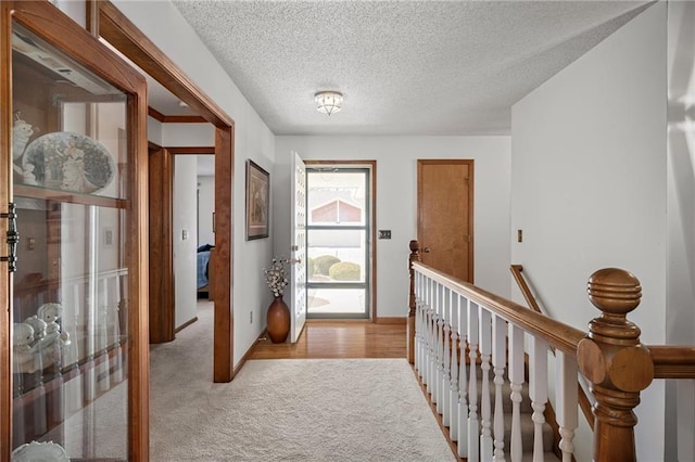 hallway with an upstairs landing, light colored carpet, a textured ceiling, and baseboards