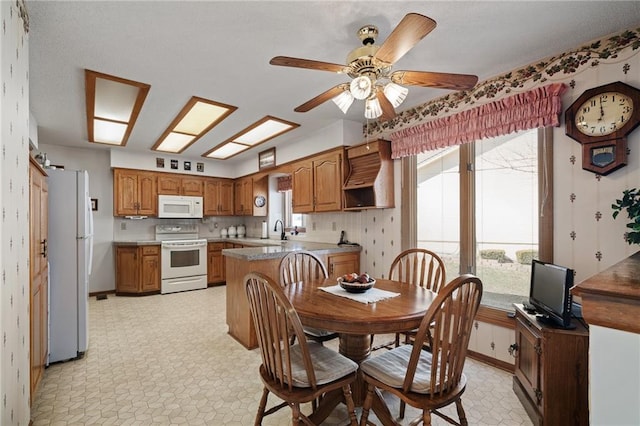 dining room featuring a skylight, light floors, baseboards, and ceiling fan