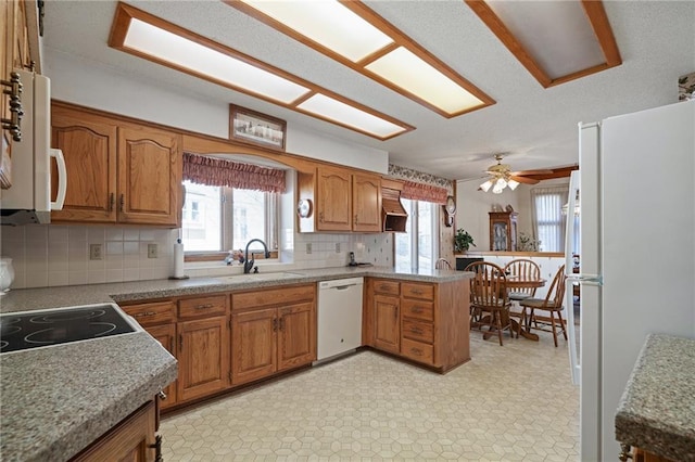 kitchen with brown cabinets, white appliances, light floors, and a sink