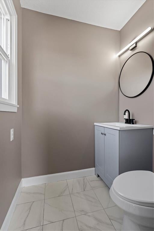 half bathroom with baseboards, toilet, marble finish floor, and vanity