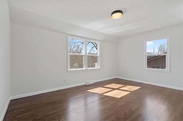 empty room with wood finished floors, a healthy amount of sunlight, visible vents, and baseboards