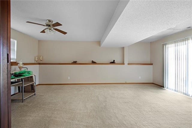 carpeted spare room featuring baseboards, a textured ceiling, a healthy amount of sunlight, and ceiling fan