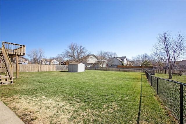 view of yard featuring a residential view, stairs, a fenced backyard, an outbuilding, and a storage unit