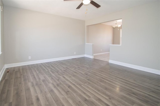 empty room featuring ceiling fan with notable chandelier, wood finished floors, and baseboards