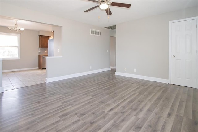 unfurnished living room with ceiling fan with notable chandelier, light wood-style floors, visible vents, and baseboards