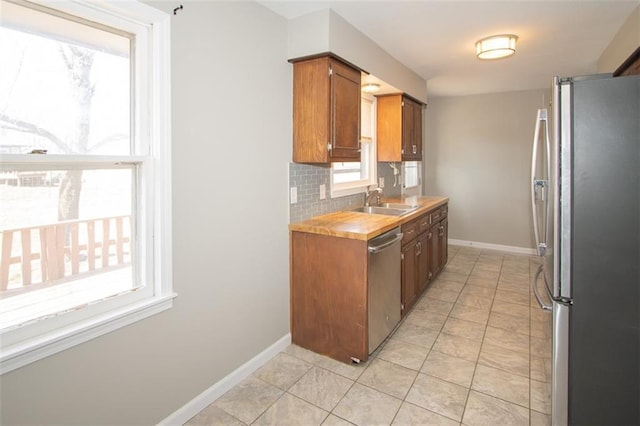 kitchen with backsplash, baseboards, light countertops, stainless steel appliances, and a sink