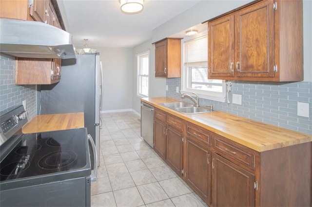 kitchen with under cabinet range hood, a sink, stainless steel appliances, decorative backsplash, and wooden counters