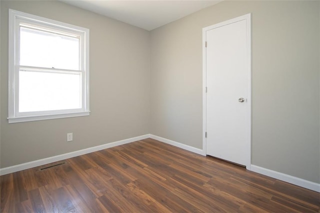 spare room with visible vents, baseboards, and dark wood-style floors