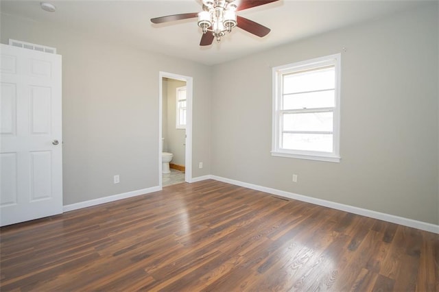 unfurnished bedroom with visible vents, connected bathroom, dark wood-type flooring, baseboards, and ceiling fan