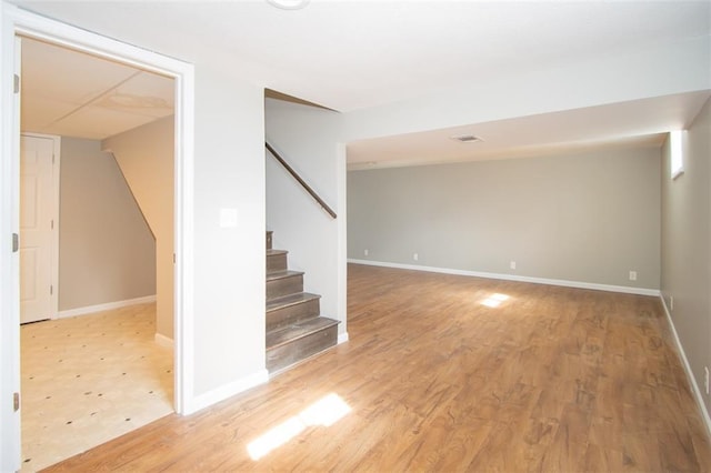 spare room featuring stairway, light wood-style flooring, and baseboards