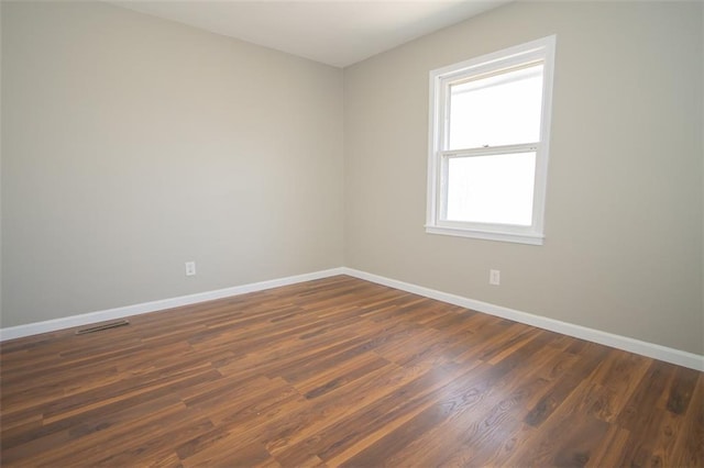 empty room with visible vents, baseboards, and dark wood finished floors