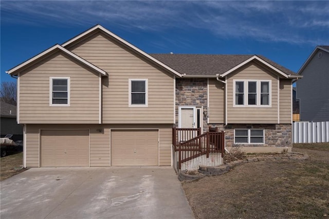 split foyer home featuring concrete driveway, a garage, stone siding, and roof with shingles