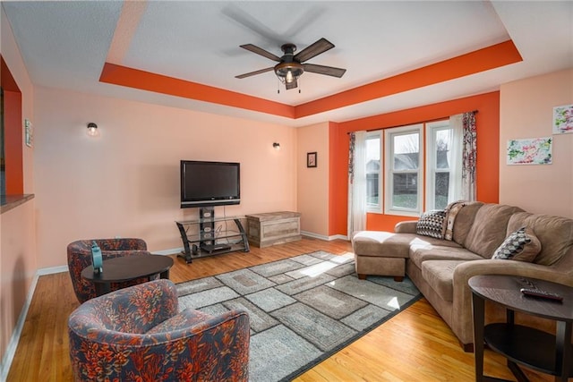 living room with ceiling fan, a tray ceiling, baseboards, and wood finished floors