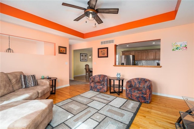 living room featuring a tray ceiling, visible vents, and wood finished floors