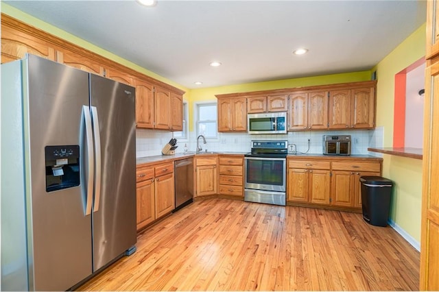 kitchen featuring light wood-style flooring, a sink, decorative backsplash, stainless steel appliances, and brown cabinets