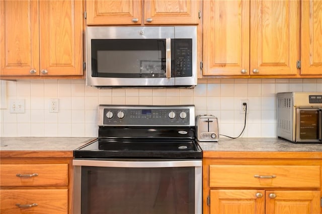 kitchen featuring tasteful backsplash, stainless steel appliances, brown cabinetry, a toaster, and light countertops