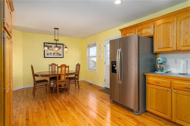 kitchen with tasteful backsplash, stainless steel fridge with ice dispenser, pendant lighting, light wood-type flooring, and brown cabinets