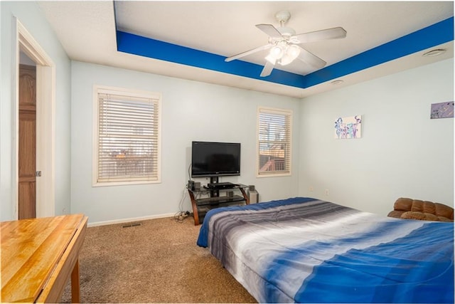 carpeted bedroom featuring ceiling fan, baseboards, and a tray ceiling