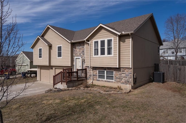 split foyer home featuring central air condition unit, driveway, stone siding, fence, and a garage