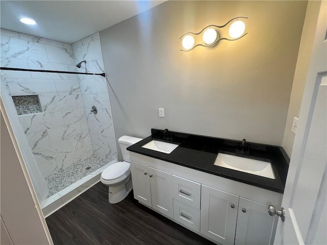 bathroom featuring a sink, tiled shower, toilet, and wood finished floors