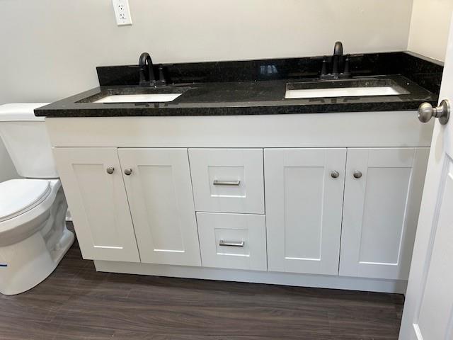 bathroom featuring a sink, toilet, wood finished floors, and double vanity