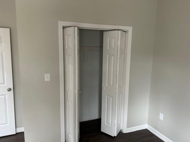 unfurnished bedroom with dark wood finished floors, baseboards, and a closet