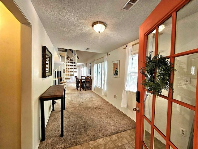 corridor with visible vents, stairway, a textured ceiling, and carpet floors