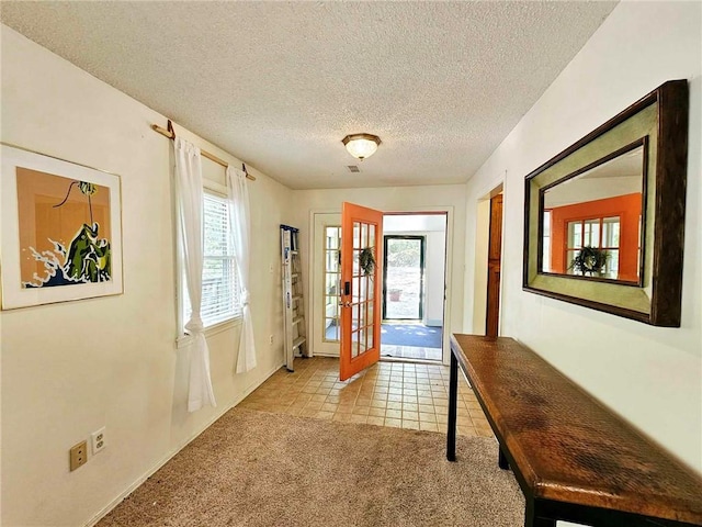 entryway with visible vents, a textured ceiling, french doors, light tile patterned floors, and light colored carpet