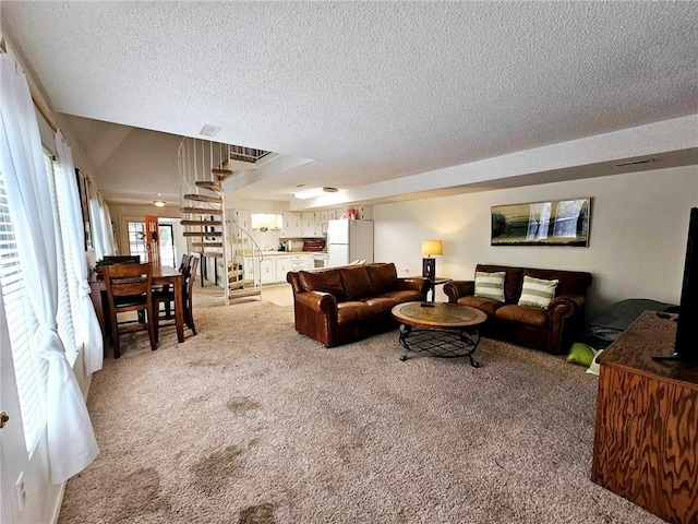 living area with light carpet, a textured ceiling, and stairs