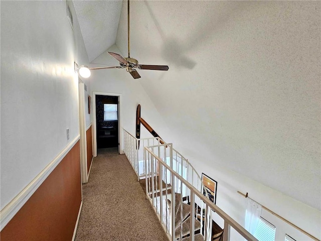 hall featuring visible vents, carpet, vaulted ceiling, an upstairs landing, and a textured ceiling