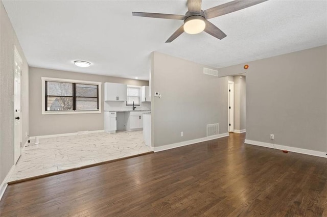 unfurnished living room with a sink, visible vents, baseboards, and wood finished floors