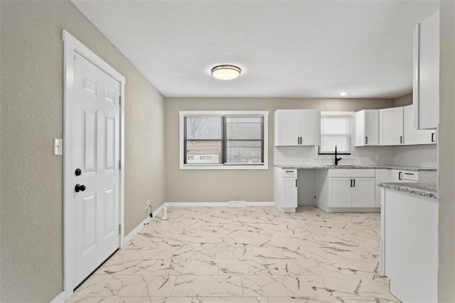 kitchen with a healthy amount of sunlight, baseboards, marble finish floor, white cabinetry, and a sink