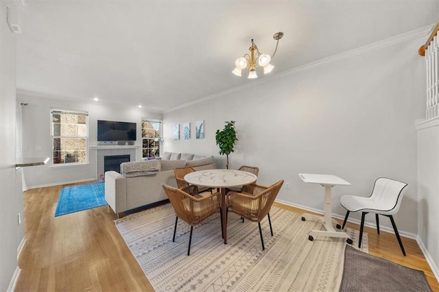 dining room featuring a fireplace, crown molding, baseboards, and wood finished floors