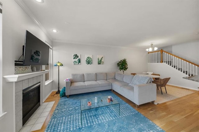 living room featuring stairway, light wood-type flooring, ornamental molding, a fireplace, and an inviting chandelier