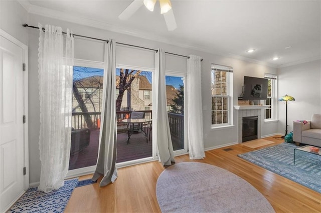 entryway with baseboards, ceiling fan, ornamental molding, a tile fireplace, and wood finished floors