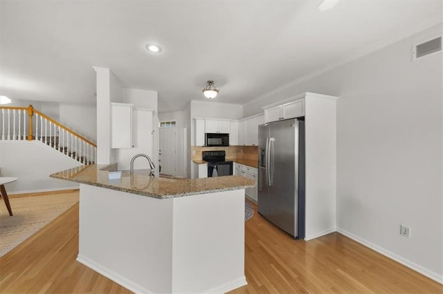 kitchen featuring black appliances, light wood-style flooring, light stone countertops, and a peninsula