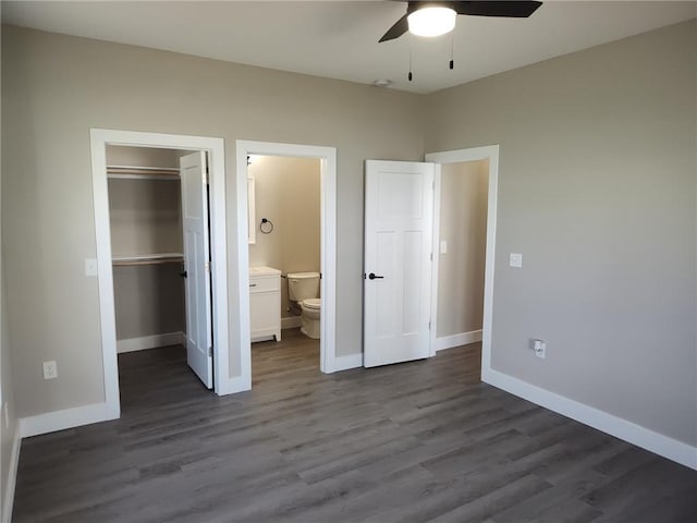 unfurnished bedroom featuring a closet, a walk in closet, baseboards, and dark wood-style flooring