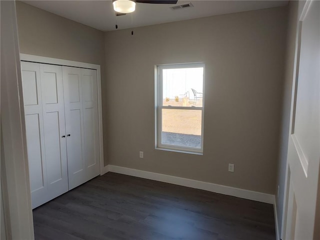 unfurnished bedroom featuring dark wood finished floors, visible vents, a closet, and baseboards