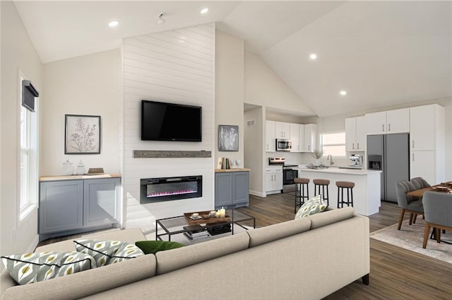 living room with a glass covered fireplace, recessed lighting, high vaulted ceiling, and dark wood-type flooring