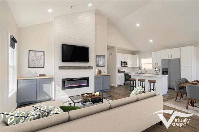 living area with a glass covered fireplace, recessed lighting, dark wood finished floors, and high vaulted ceiling