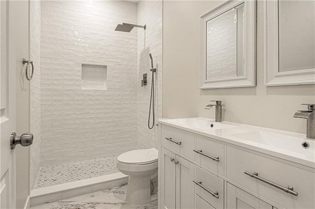 bathroom featuring double vanity, toilet, a tile shower, and a sink