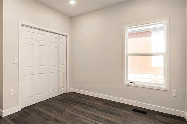 unfurnished bedroom featuring visible vents, baseboards, a closet, and dark wood finished floors