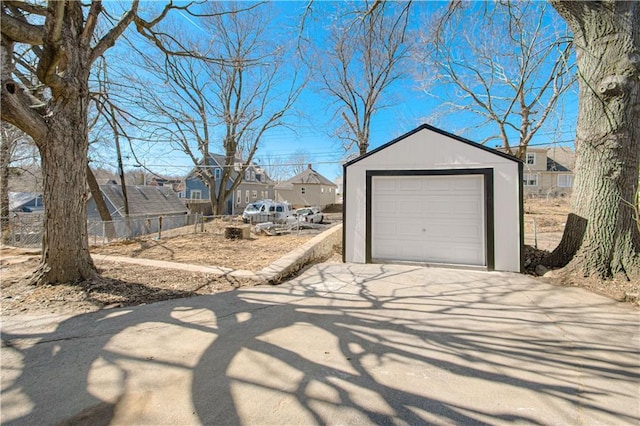 detached garage featuring a residential view, driveway, and fence